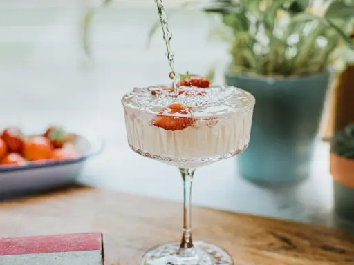 Un cocktail sans alcool surprenant, avec des fraises fraîches, est préparé. Des plantes vertes en arrière-plan ajoutent une touche de nature.