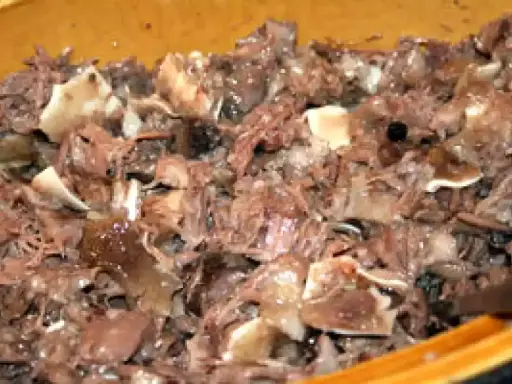 Un plat de fromage de tête, avec des morceaux de viande et de cartilage, dans un récipient en bois.
