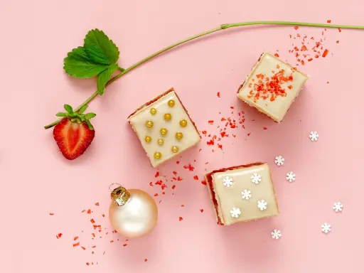 Délicieux petits fours sucrés, parfaits pour une recette de fête. Une fraise, une boule de Noël et des paillettes rouges complètent la scène.