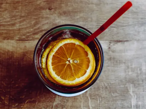 Verre de boisson sans alcool pour accompagner repas, avec rondelles d'orange et glaçons, sur fond de bois.
