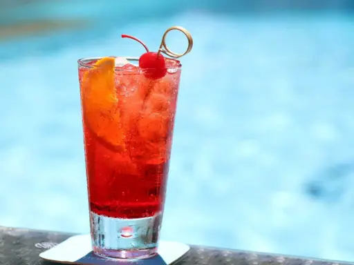Un cocktail sans alcool à préparer la veille, garni d'une cerise et d'une tranche d'orange, prêt à être dégusté au bord de la piscine.