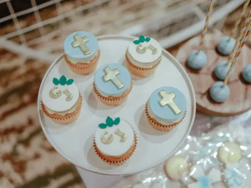 Jolis cupcakes décorés de croix dorées et de lettres pour un buffet dessert baptême. Des cake pops bleus sont aussi présents.