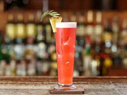 Un cocktail rouge vif, garni d'ananas, sur un bar. Idéal pour un cocktail pas cher pour 10 personnes, facile à préparer.