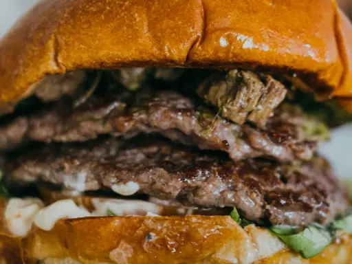Gros plan sur un steak burger double, avec des steaks juteux, de la sauce et de la laitue entre deux pains briochés dorés.