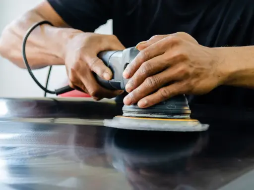 Mains polissant une surface sombre avec une ponceuse orbitale pour polir aluminium rayé.