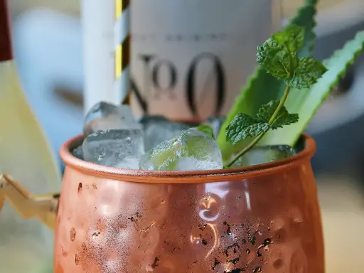 Un Moscow Mule rafraîchissant dans sa tasse en cuivre, garni de menthe et d'une tranche d'agrume.