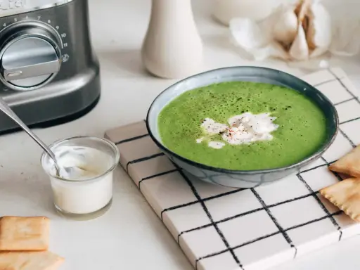 Une délicieuse soupe de légumes variés, onctueuse et verte, garnie de crème et servie avec des crackers.