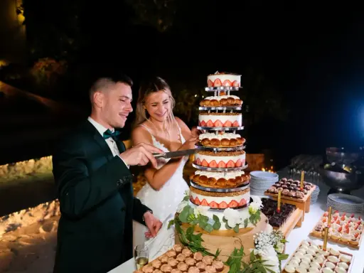 Un couple coupe un dessert mariage original, une tour de gâteaux aux fraises et à la crème, lors d'une réception nocturne.