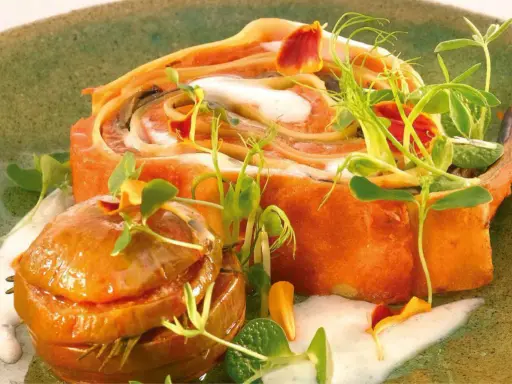 Un roulé de pâtes orange, garni de crème et de pousses, avec une petite boule caramélisée. Un plat qui rappelle les "maccheroni della mamma".