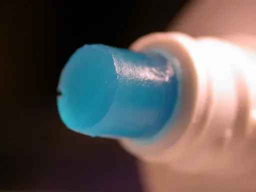 Goutte de dentifrice bleu sortant d'un tube blanc, parfaite pour polir l'aluminium.