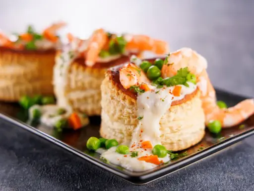 Trois bouchées de tapas crevette, garnies de crevettes, petits pois et sauce crémeuse, sur un plateau noir.
