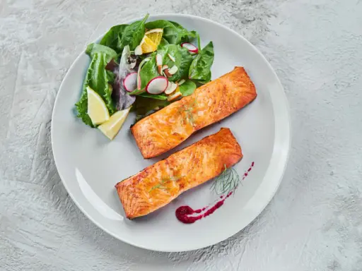 Deux pavés de saumon au four, accompagnés d'une salade fraîche et de quartiers de citron. Un délice simple et savoureux.