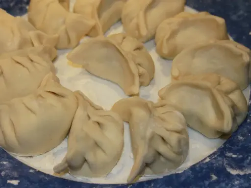 Assiette de ravioli pekinois crus, prêts à être cuisinés. La pâte est fine et plissée, prête à accueillir une garniture savoureuse.