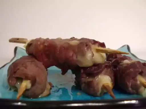 Brochettes de boeuf roulées autour de fromage fondant, servies sur une assiette bleue.