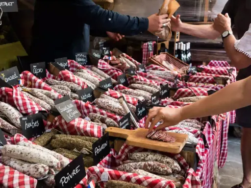 Vitrine de charcuterie avec de nombreuses saucisses et un client qui en choisit une tranche.