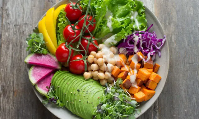 Un bol coloré avec avocat, tomates, pois chiches, patates douces, chou rouge, radis et poivron jaune. Parfaites salades originales pour buffet.