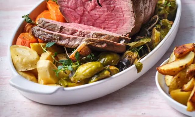 Tranches de rosbeef froid, accompagnées de pommes de terre rôties, carottes et choux de Bruxelles dans un plat blanc.