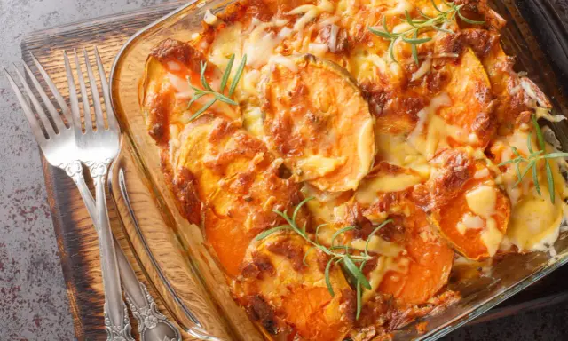 Gratin de patates douces au fromage, prêt pour un repas d'anniversaire. Deux fourchettes argentées sont posées sur le côté.