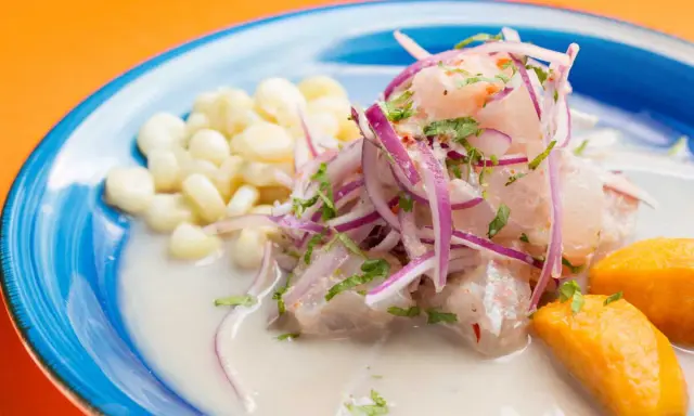 Ceviche frais baignant dans un leche de tigre crémeux, garni d'oignons rouges, de coriandre, de maïs et de patate douce.