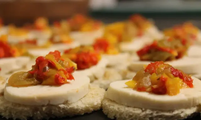 Petits toasts pour l'apéro, garnis de fromage blanc et d'une préparation colorée de poivrons et oignons.