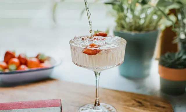 Un cocktail sans alcool surprenant, avec des fraises fraîches, est préparé. Des plantes vertes en arrière-plan ajoutent une touche de nature.
