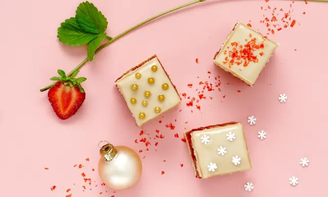Délicieux petits fours sucrés, parfaits pour une recette de fête. Une fraise, une boule de Noël et des paillettes rouges complètent la scène.