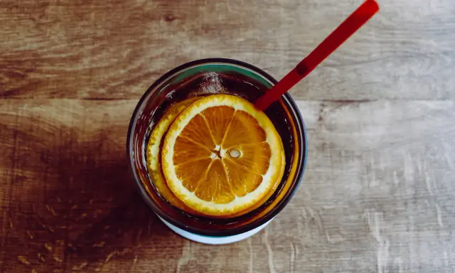 Verre de boisson sans alcool pour accompagner repas, avec rondelles d'orange et glaçons, sur fond de bois.