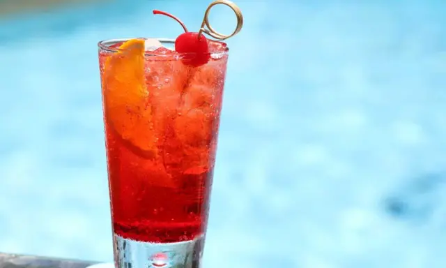 Un cocktail sans alcool à préparer la veille, garni d'une cerise et d'une tranche d'orange, prêt à être dégusté au bord de la piscine.