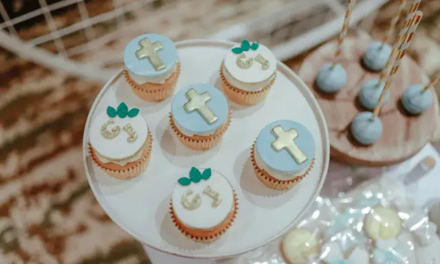 Jolis cupcakes décorés de croix dorées et de lettres pour un buffet dessert baptême. Des cake pops bleus sont aussi présents.