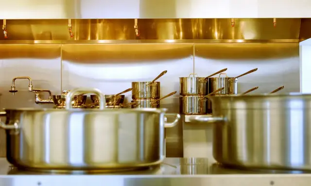 Une cuisine professionnelle avec des casseroles en acier inox 18/10 étincelantes. Des robinets chromés et des gicleurs de sécurité complètent l'ensemble.