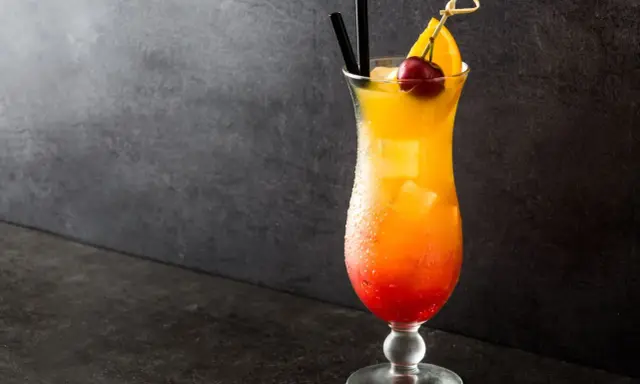 Cocktail Sex on the Beach recette 5l, dégradé rouge-orange, garni d'une cerise et d'une tranche d'orange.