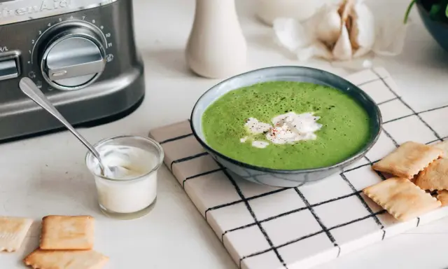 Une délicieuse soupe de légumes variés, onctueuse et verte, garnie de crème et servie avec des crackers.