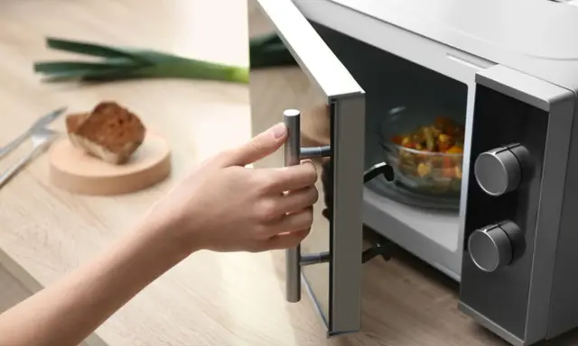 Main tenant ouvre son micro-ondes pour y placer un plat. La question est : peut-on mettre de l'inox au micro-onde ?
