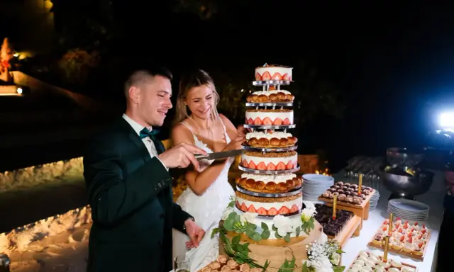 Un couple coupe un dessert mariage original, une tour de gâteaux aux fraises et à la crème, lors d'une réception nocturne.
