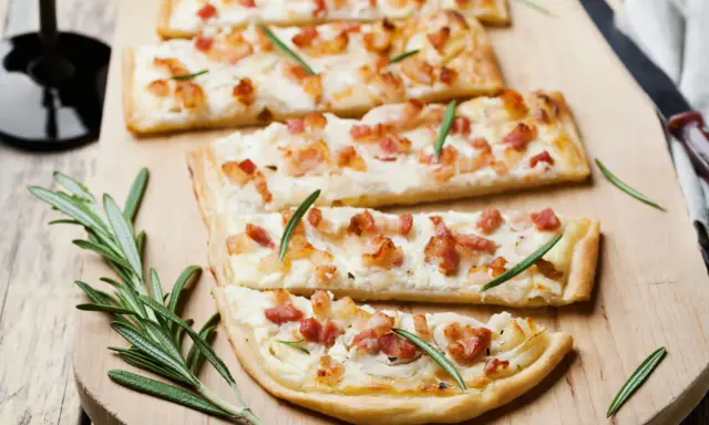 Quatre tartes flambées, une délicieuse entrée alsacienne, garnies de lardons et de romarin sur une planche en bois.