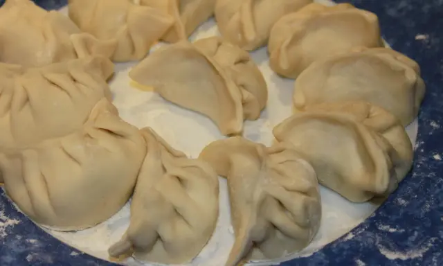 Assiette de ravioli pekinois crus, prêts à être cuisinés. La pâte est fine et plissée, prête à accueillir une garniture savoureuse.