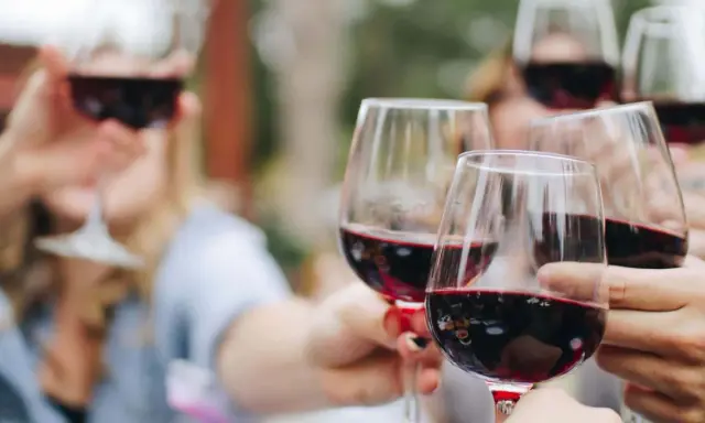 Des verres de vin rouge levés en toast. Pour 40 personnes, combien de bouteille de vin prévoir ? Environ 15 à 20 bouteilles.