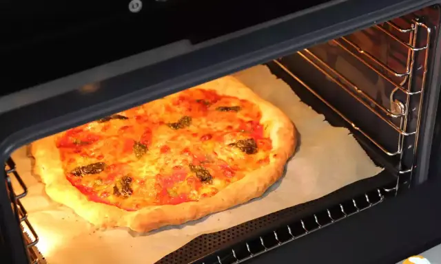 Une pizza dorée cuit dans un four, sa croûte gonflée et son fromage fondant témoignent de la parfaite fonction pizza four.