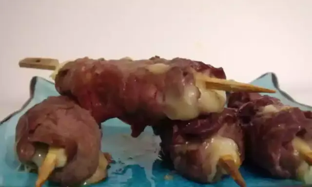 Brochettes de boeuf roulées autour de fromage fondant, servies sur une assiette bleue.