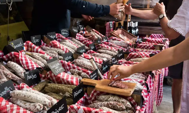 Vitrine de charcuterie avec de nombreuses saucisses et un client qui en choisit une tranche.