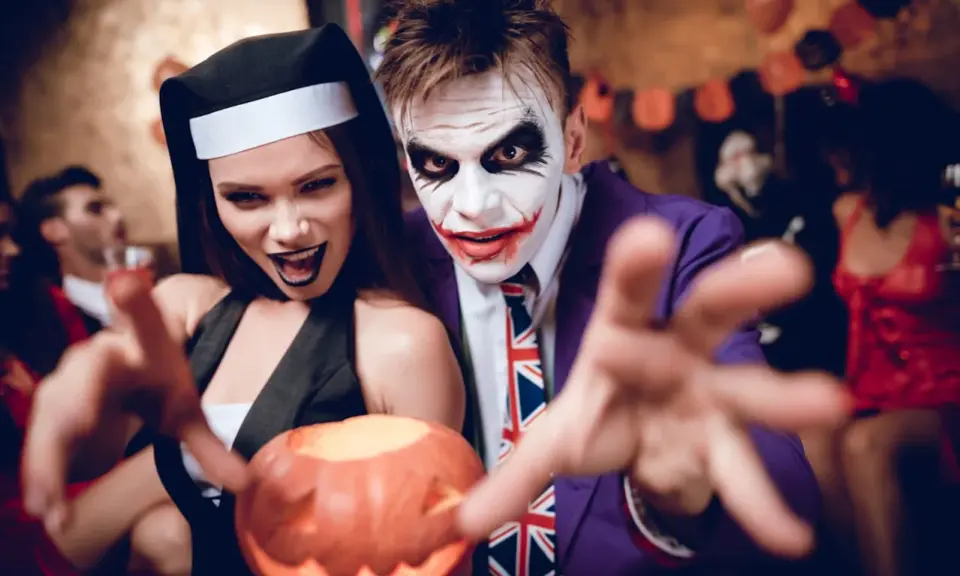 Un couple en costumes effrayants, une nonne et le Joker, profite d'une **soirée costumée** d'Halloween, tenant une citrouille sculptée.