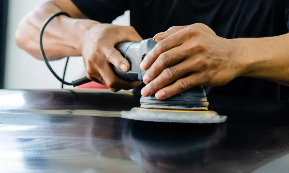Mains polissant une surface sombre avec une ponceuse orbitale pour polir aluminium rayé.