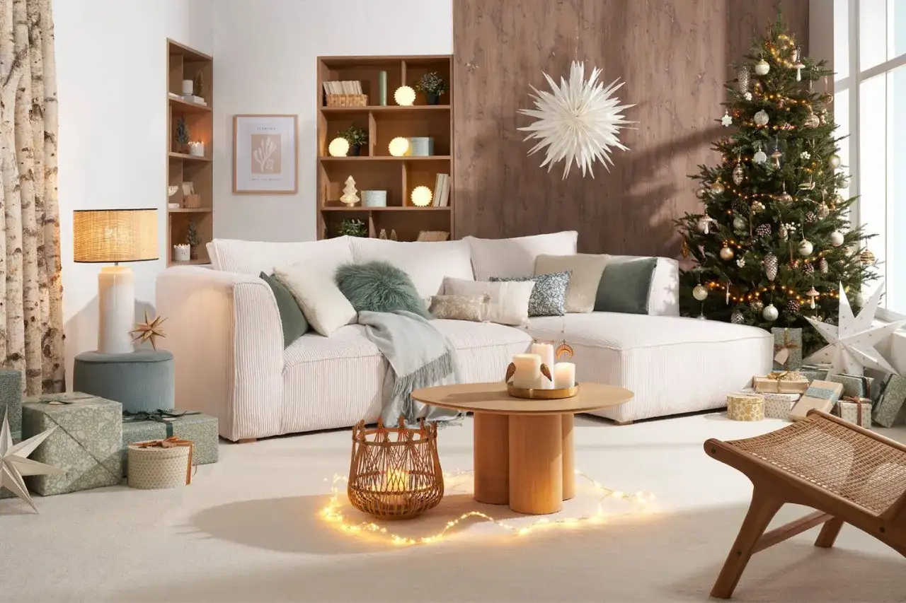 Un salon cosy prêt pour organiser une crémaillère de Noël. Sapin décoré, cadeaux emballés, bougies et guirlandes lumineuses créent une ambiance chaleureuse.