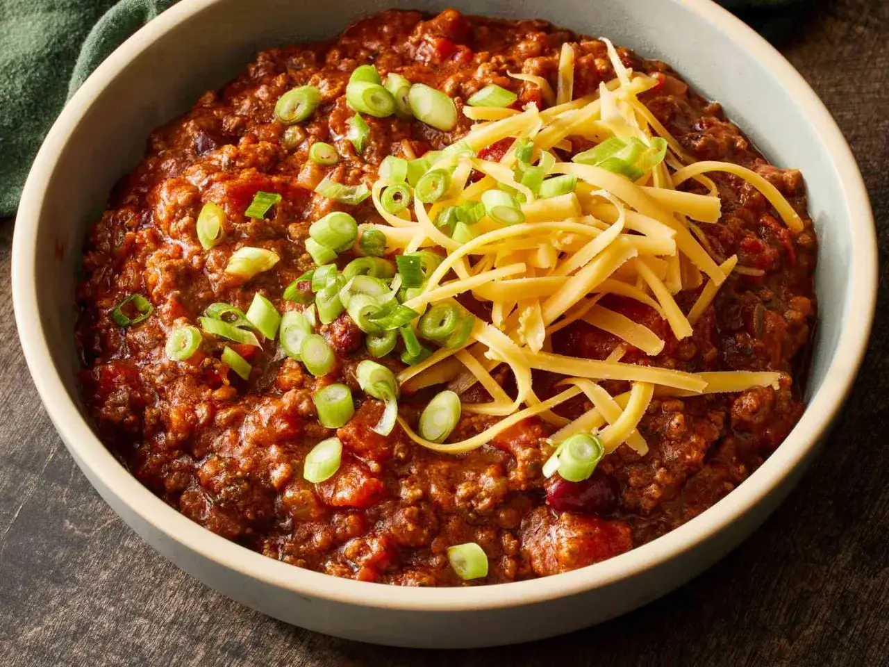 Un bol de chili con carne, garni de fromage râpé et d'oignons verts. Une recette de chef qui réchauffe le cœur.