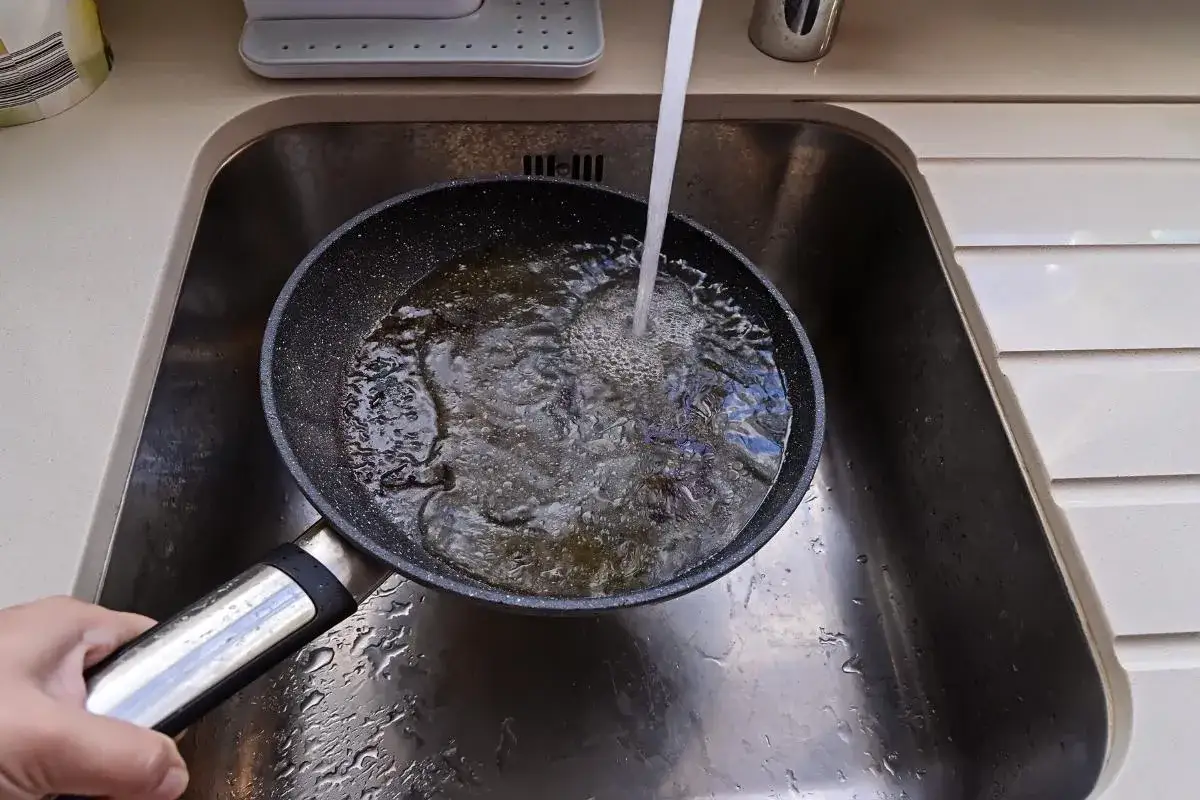 Maintenant, je vais nettoyer le dessous du poêle. L'eau coule dans l'évier, remplissant la poêle.