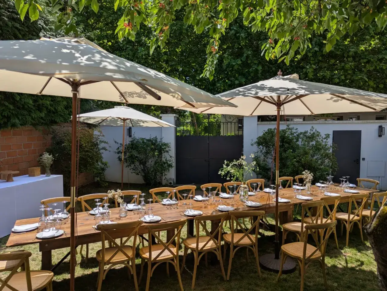 Table dress&eacute;e pour un pique-nique chic sous les parasols, avec des chaises en bois et des verres &eacute;tincelants.