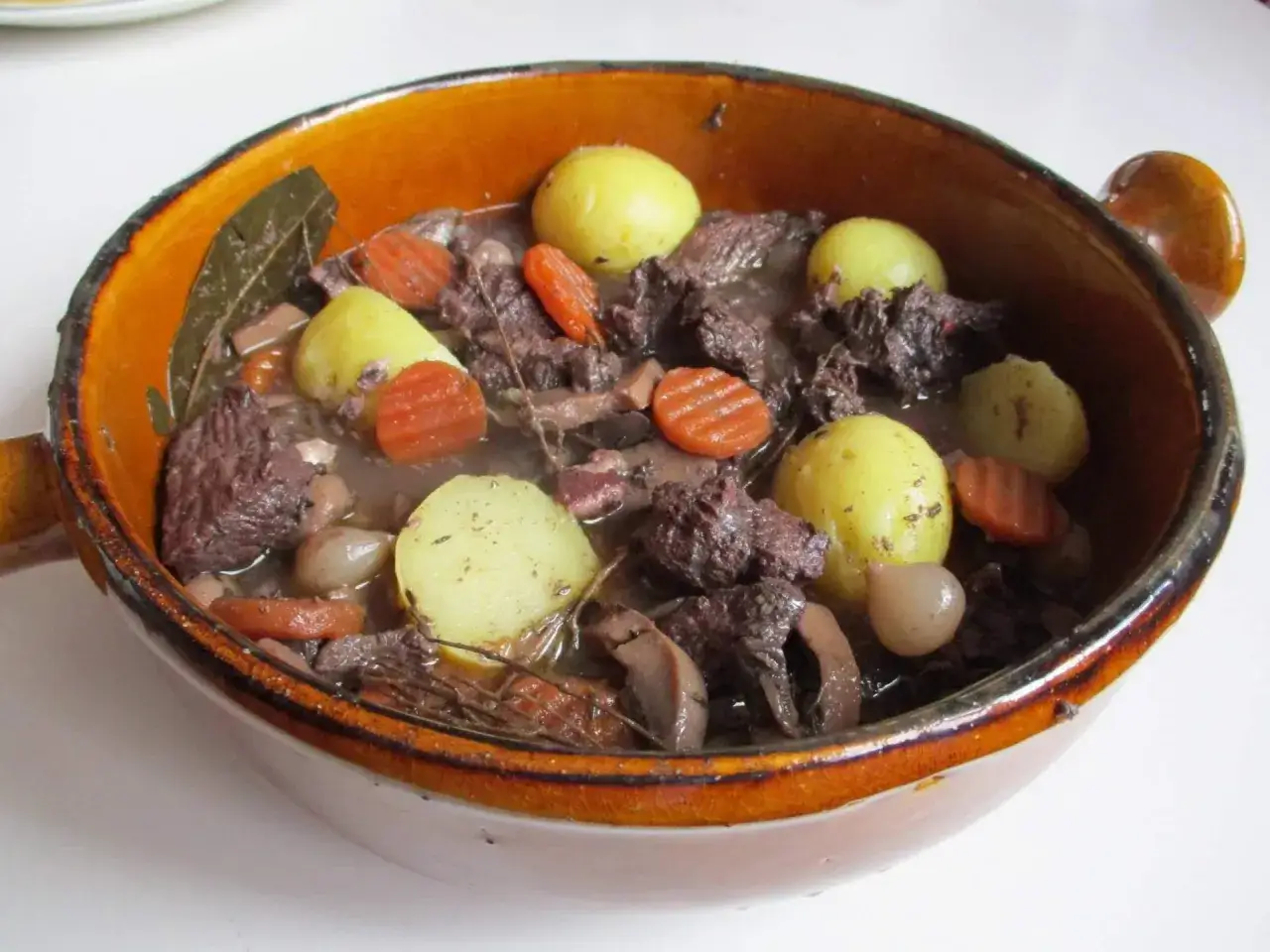 Un plat en terre cuite d&eacute;bordant d'un savoureux repas proven&ccedil;al : morceaux de b&oelig;uf mijot&eacute;s, pommes de terre, carottes et oignons.
