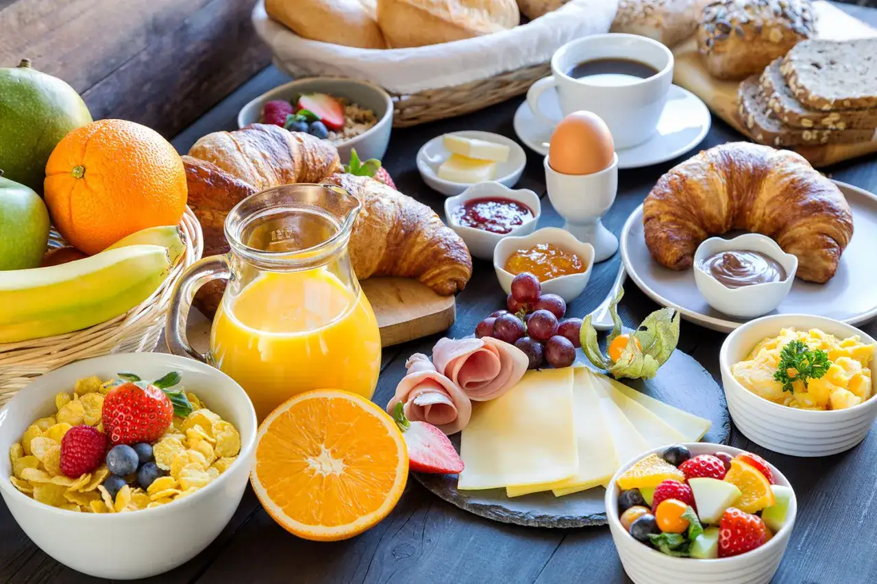 Un délicieux buffet petit déjeuner avec croissants, jus d'orange, fruits frais, œufs, café et pain.