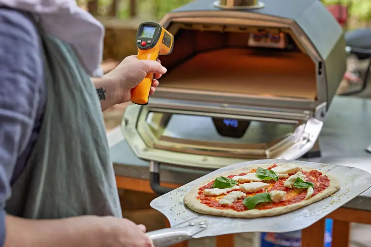 Une personne vérifie la température d'un four à pizza avec un thermomètre infrarouge avant de cuire une pizza margherita.