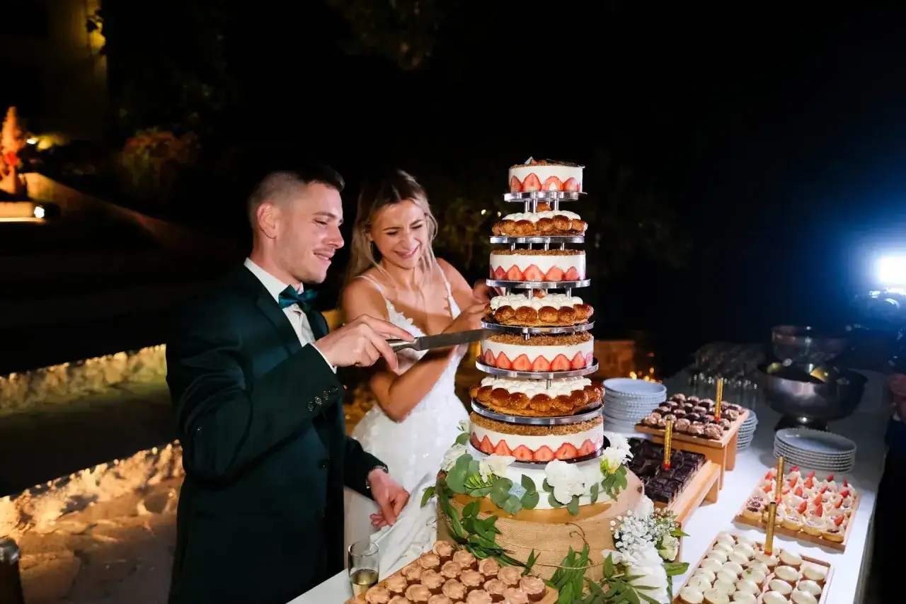 Un couple coupe un dessert mariage original, une tour de g&acirc;teaux aux fraises et &agrave; la cr&egrave;me, lors d'une r&eacute;ception nocturne.